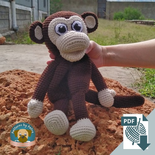 The finished crochet monkey lovey, Charlie, sitting on an orange rock while being supported by Patsy.