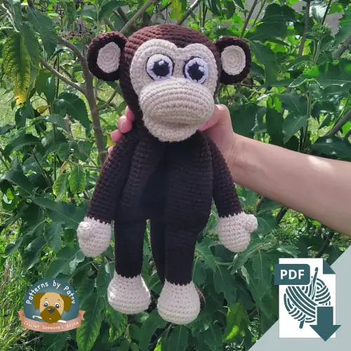 Crochet monkey lovey with long arms and legs, held in front of green leaves.