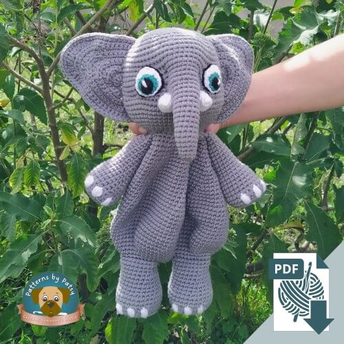 Ellie the grey amigurumi crochet elephant lovey pattern held outdoors against green leaves