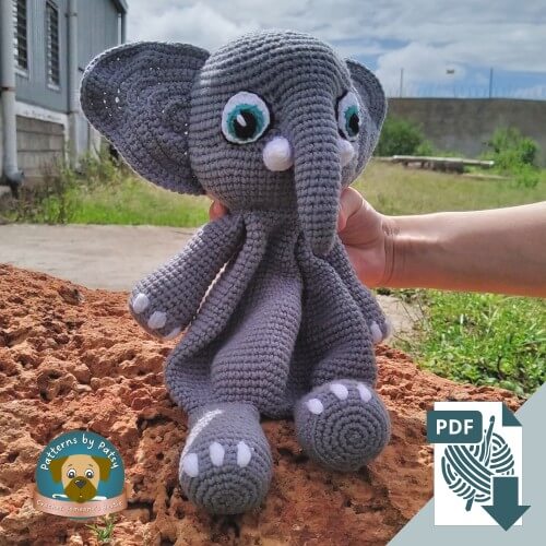 The finished crochet elephant lovey pattern sitting on a rock outdoors.