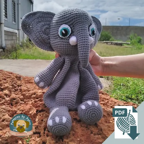 The finished crochet elephant lovey pattern sitting on a rock outdoors.