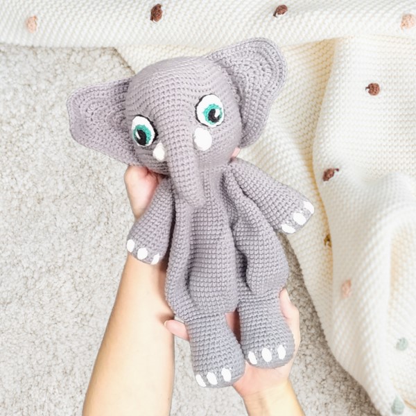 Crocheted elephant lovey being held over a baby blanket, showcasing the finished result of a digital amigurumi crochet pattern.